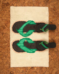 A pairs of black and green flip-flops on a textured bath mat with flip flop design on a cork-like background.