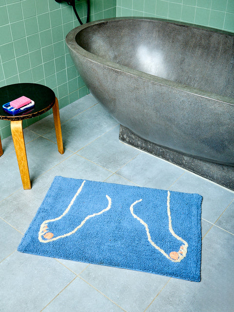 Blue bath mat with footprints on a bathroom floor next to a bathtub.