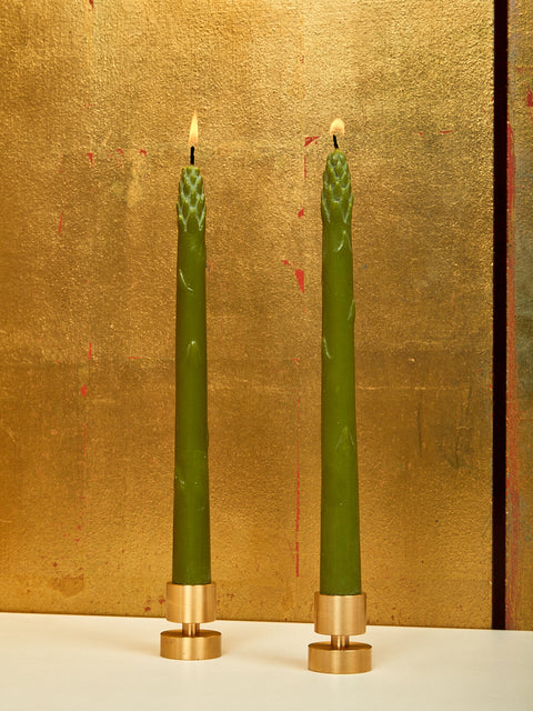 A pair of lit asparagus shaped dinner candles in small brass holders.