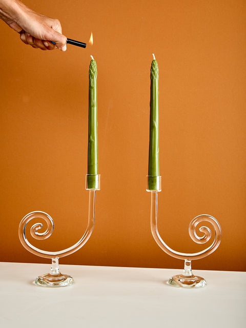 Person lighting two green candles in decorative glass candle holders against a brown background