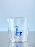 Clear glass tumbler with a blue goose figurine on a light blue background
