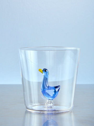 Clear glass tumbler with a blue goose figurine on a light blue background