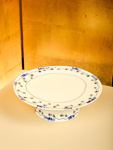 Decorative ceramic cake stand with floral patterns on a stand against a gold background