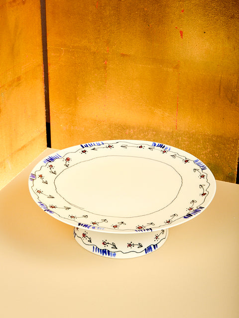 Decorative ceramic cake stand with floral patterns on a stand against a gold background