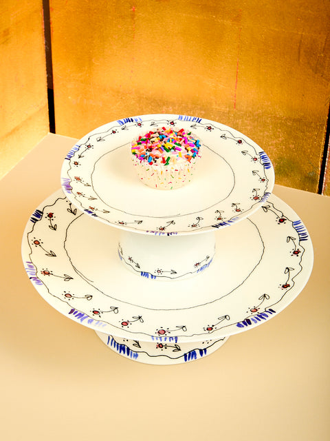 Two stacked decorative cake stands with a small cake on a gold background
