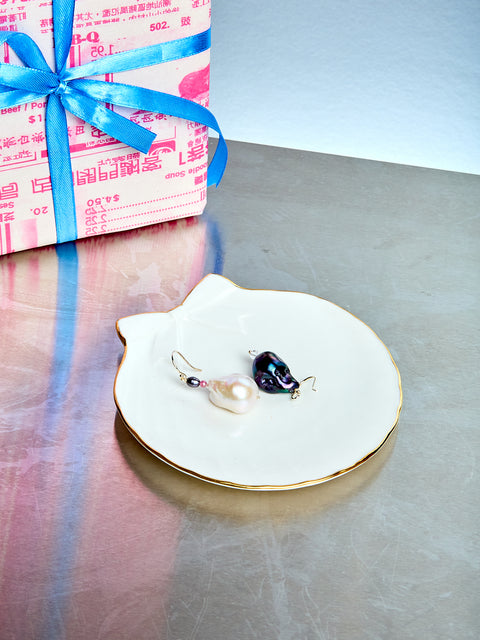 Jewelry dish with earrings on a reflective surface next to a wrapped gift.