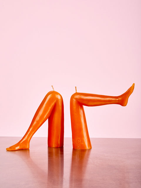 Orange candle shaped like legs on a pink background