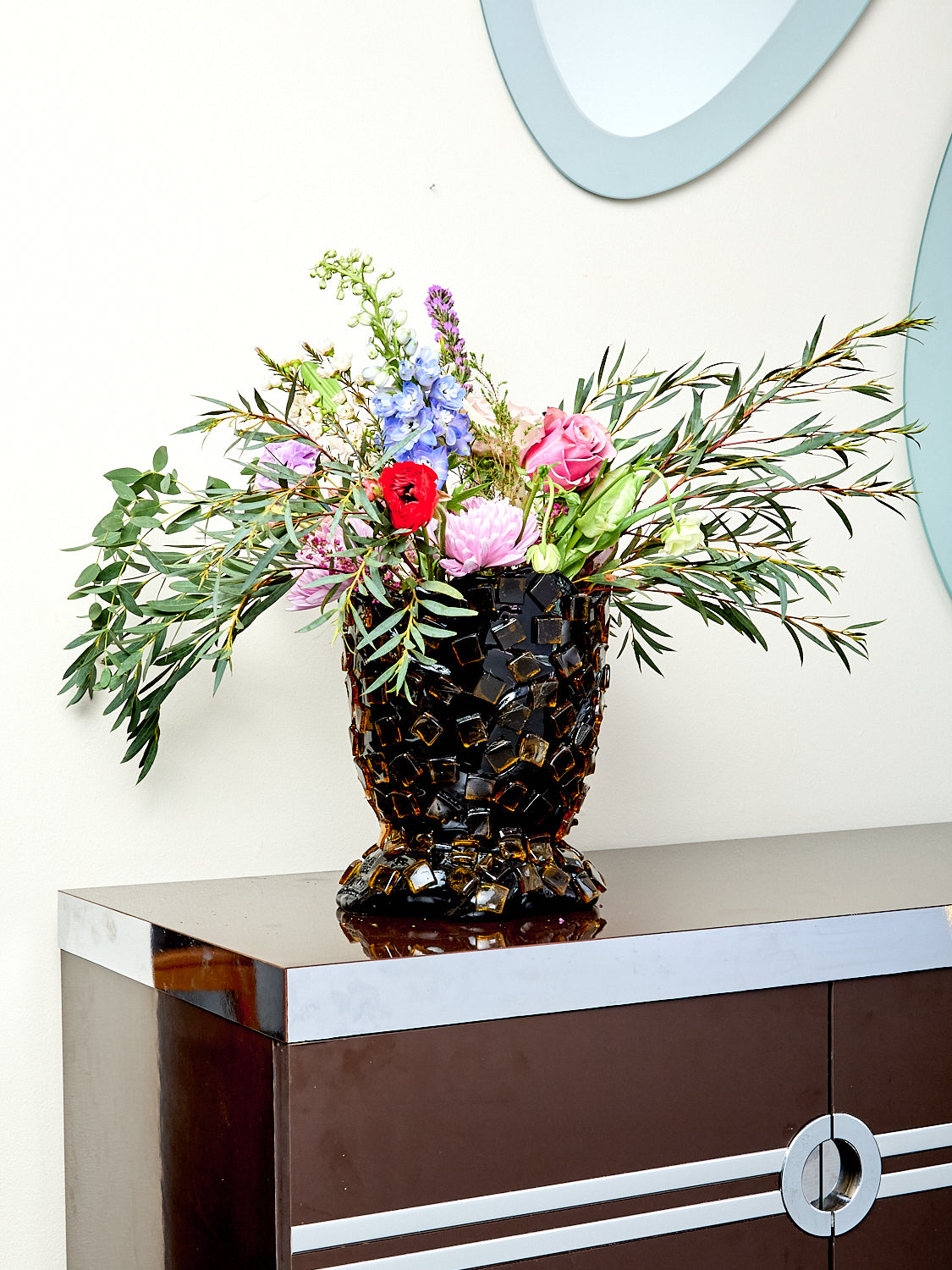Decorative resin vase with mosaic tile design, holding flowers.