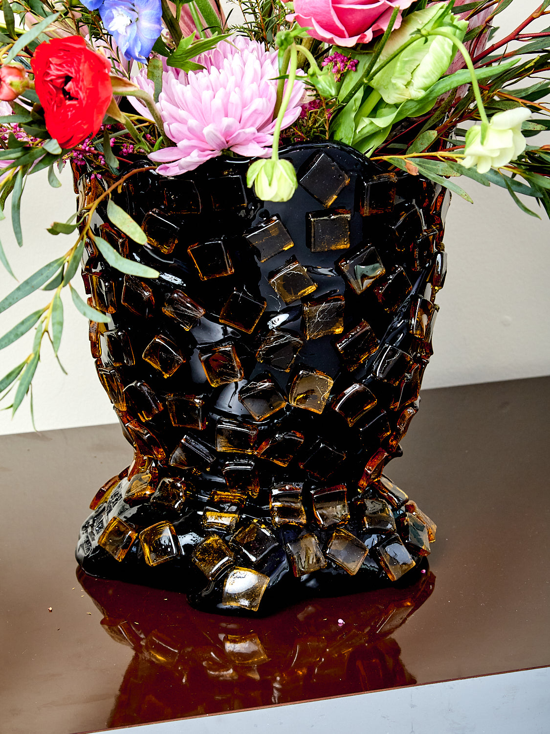 Decorative resin vase with mosaic tile design, holding flowers.