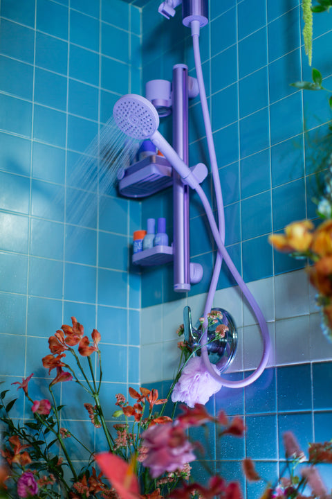 Lavender shower set against a blue tiled wall with flowers in the foreground