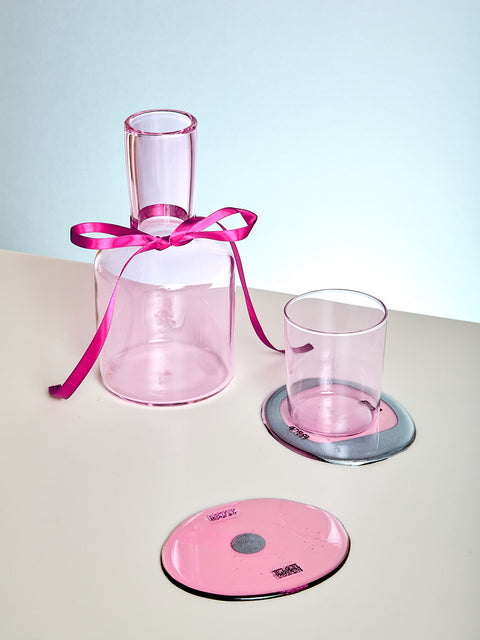 Pink glass carafe with a matching glass and coaster on a light surface.