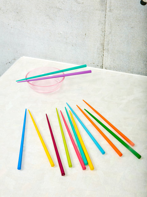Rainbow Chopsticks by Moma splayed out on a table top, a pair of teal and purple chopsticks rests on a small pink bowl.